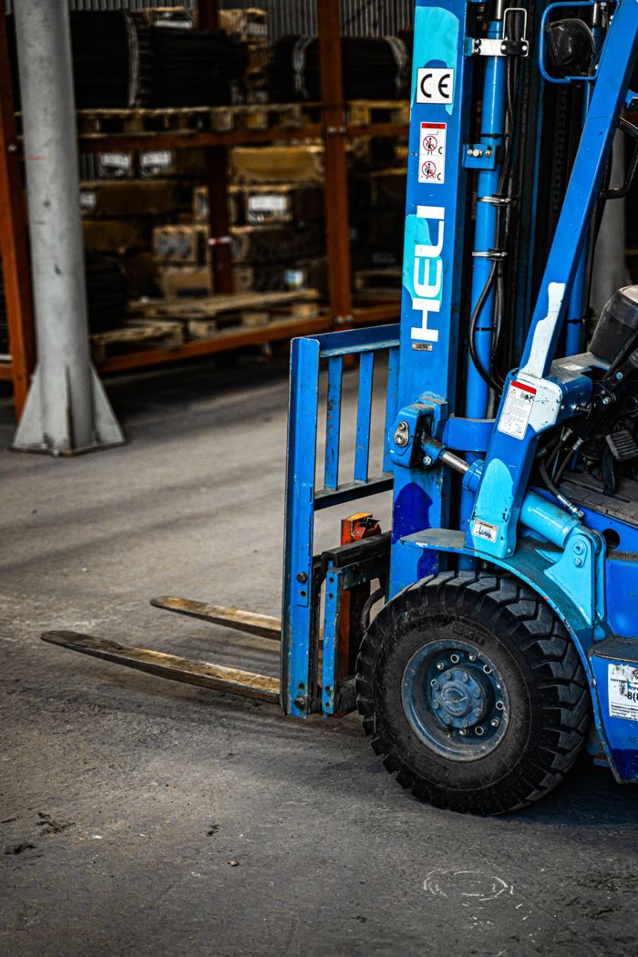 Home Blue forklift inside an industrial warehouse, parked near shelves with various items.