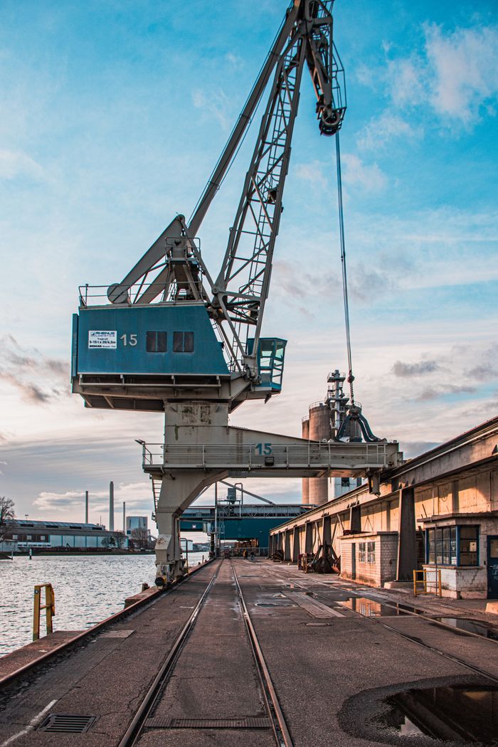 Vertical shot of a harbor crane by industrial warehouses during the day.