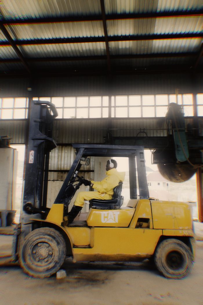 A worker in protective gear drives a forklift inside an industrial warehouse.